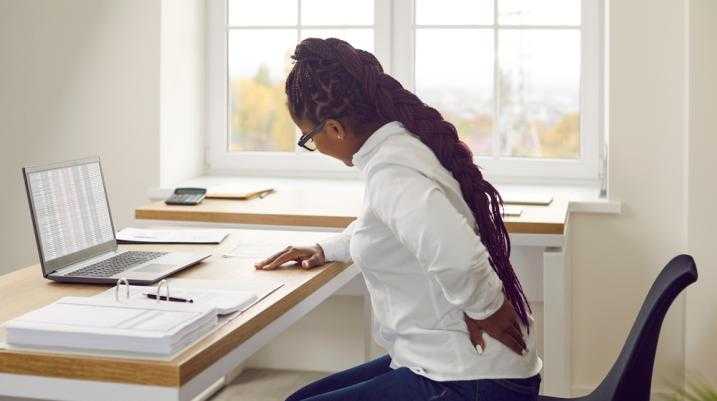 Woman at her desk holding back in pain