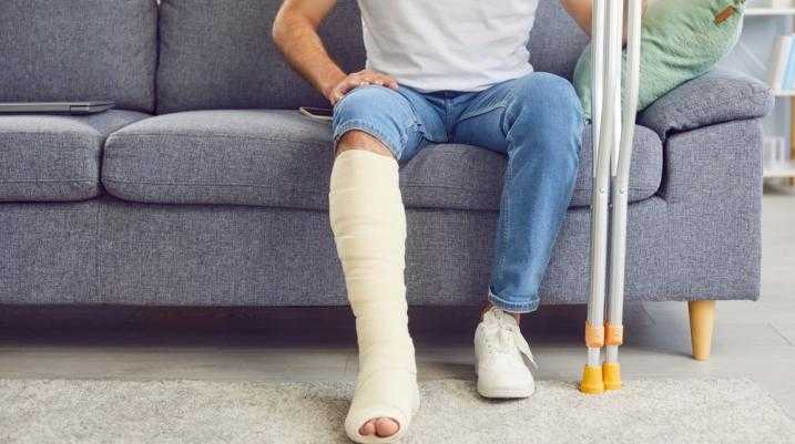 Man sitting on a couch with a leg cast holding crutches