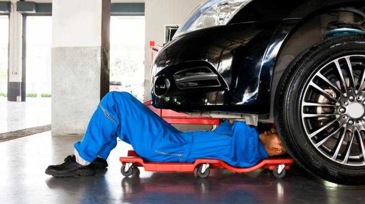 Mechanic wearing a blue jumpsuit working under a car