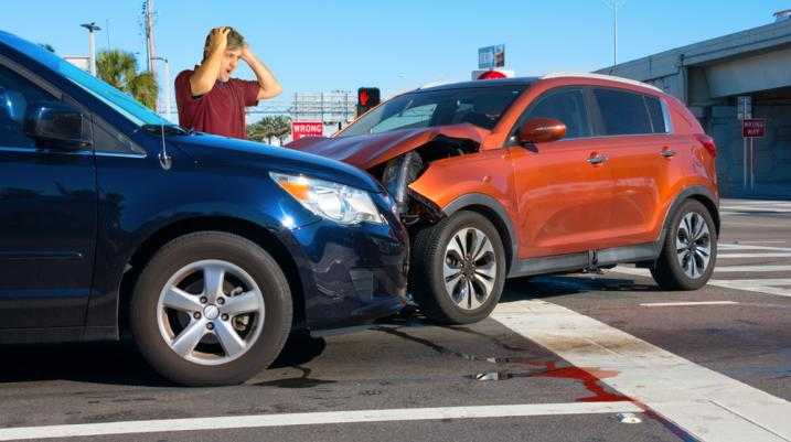 Orange and blue car crashed into each other with a man standing nearby in shock