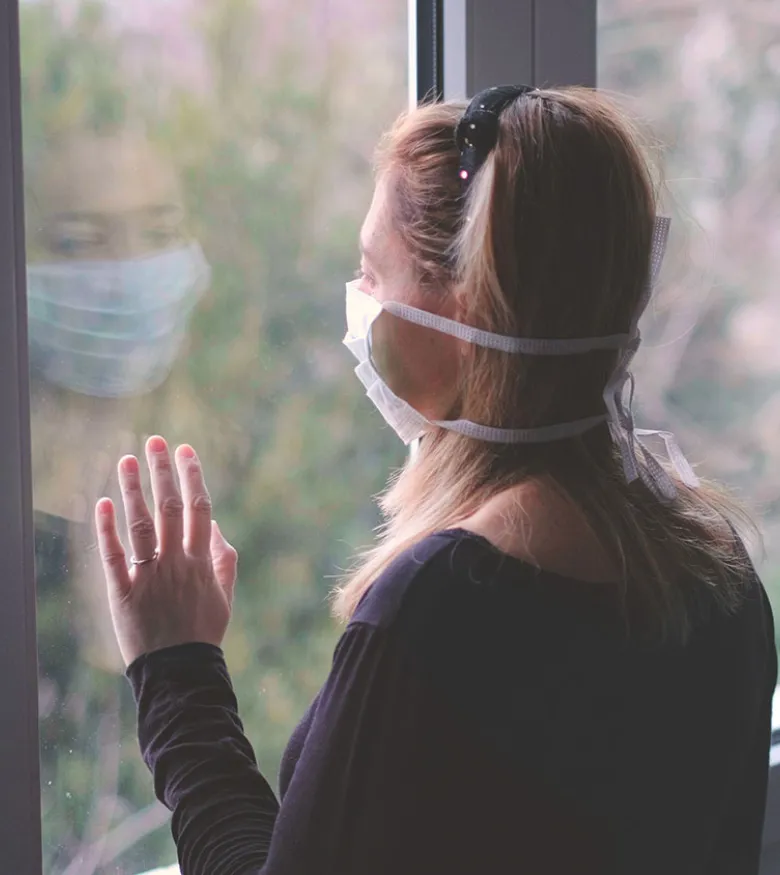 Woman in mask looking out window