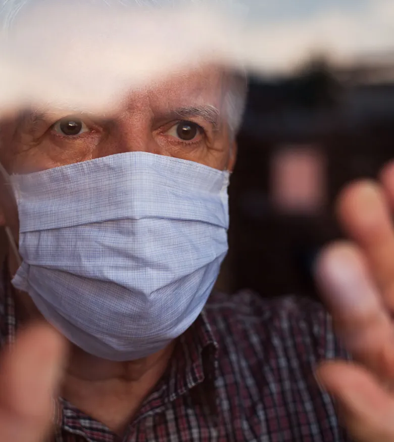 Older man behind window with mask on