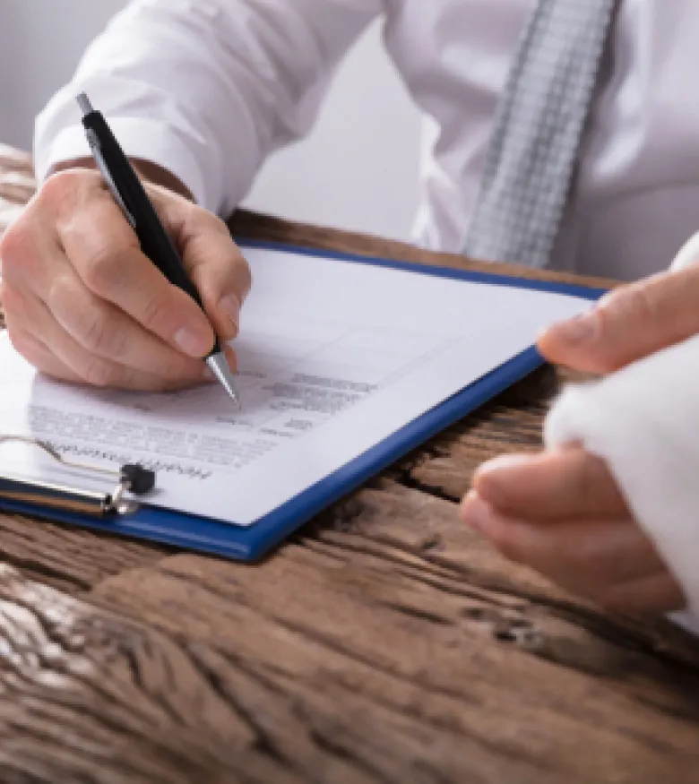 Injured worker with bandaged hand filling out paperwork at a desk, representing the need for a Workers' Compensation Attorney in Columbus.