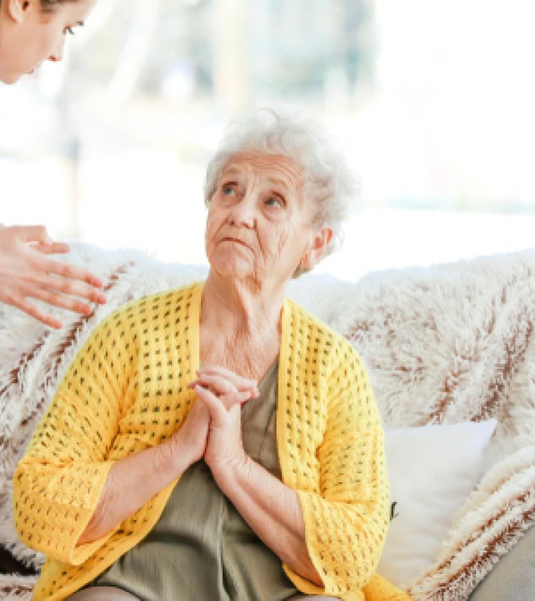 An elderly woman looking distressed while sitting on a couch, highlighting the need for a Nursing Home Abuse Lawyer in Augusta to provide legal assistance.