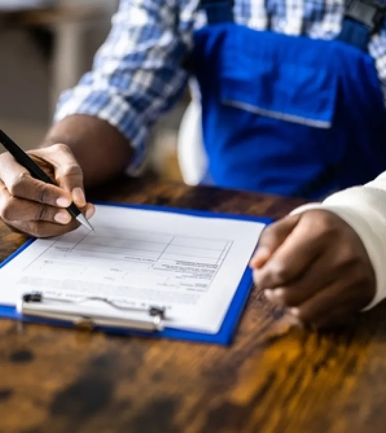 A person with an injured wrist, wrapped in a bandage, fills out paperwork on a clipboard, illustrating the need for a Workers' Compensation Attorney in Augusta.