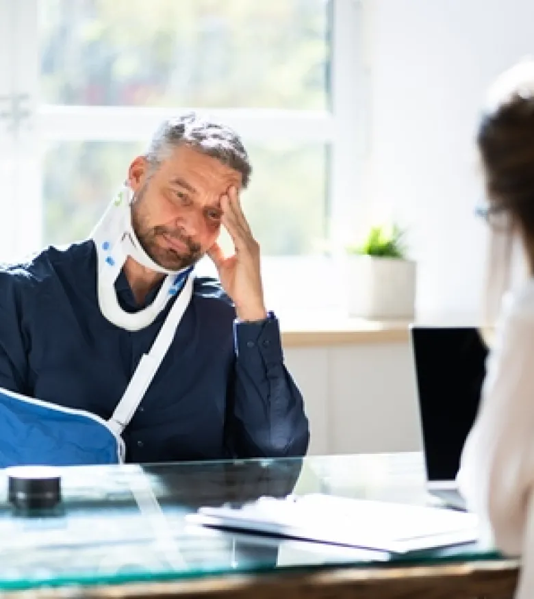 A man with a neck brace and arm sling consulting with a lawyer, highlighting the need for an Injury Lawyer in Marietta to provide legal assistance.