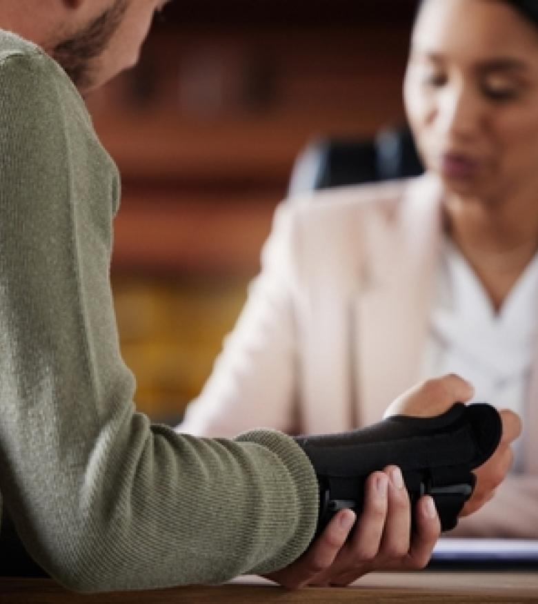A lawyer consulting with a person wearing a wrist brace, highlighting the need for an Injury Lawyer in Bowling Green to provide legal assistance.