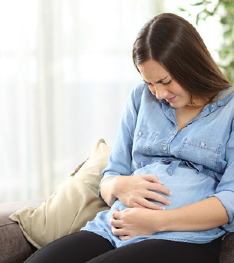 Pregnant woman in pain sitting on a couch, consult a birth injury lawyer in The Bronx.