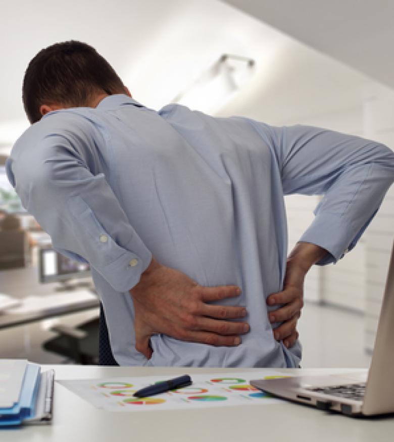 A man holding his lower back in pain while working at a desk, emphasizing the need for legal assistance for Neck, Spinal Cord, and Back Injury in Gainesville.