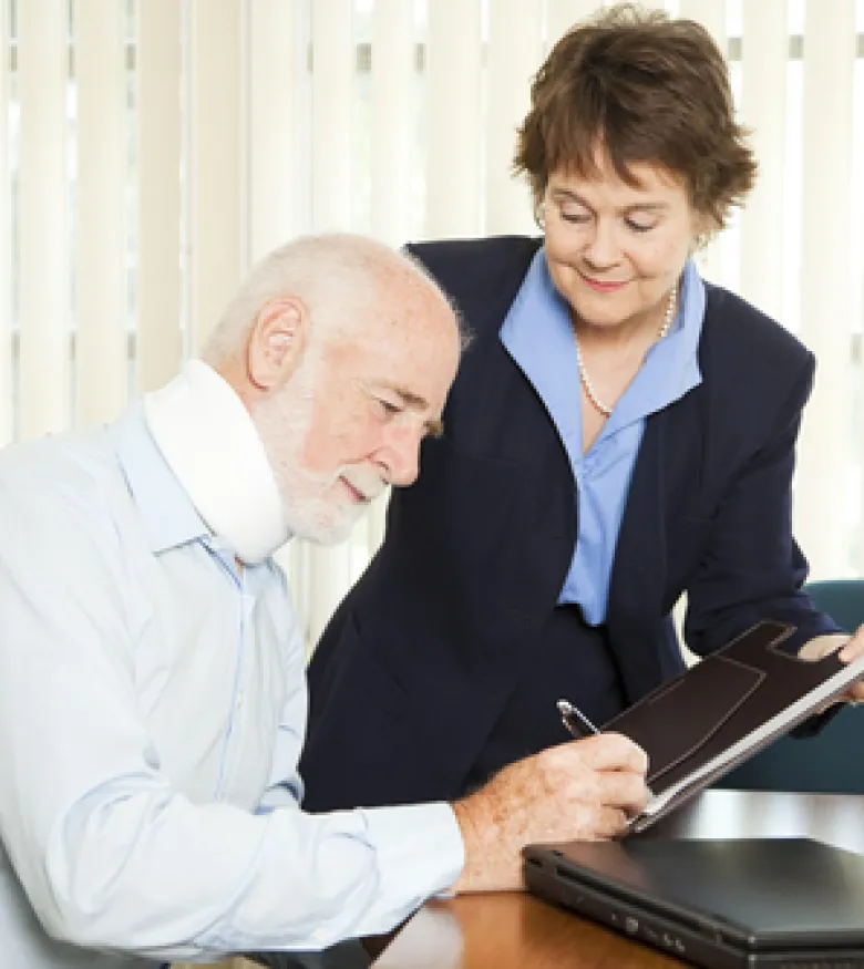 An elderly man wearing a neck brace consulting with a lawyer, highlighting the need for an Injury Lawyer in Covington to provide legal assistance.