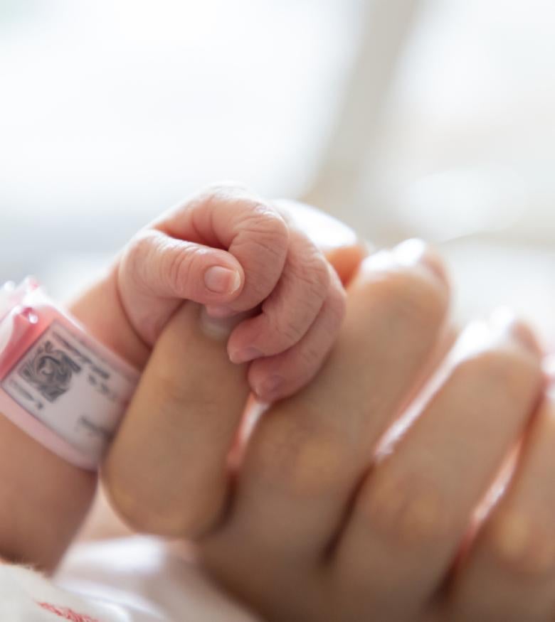 Newborn baby grasping adult's finger with hospital ID bracelet in focus