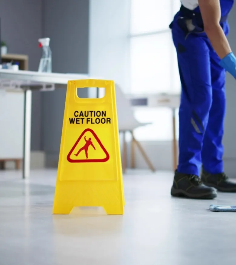 Janitor mopping floor next to yellow caution wet floor sign in office setting