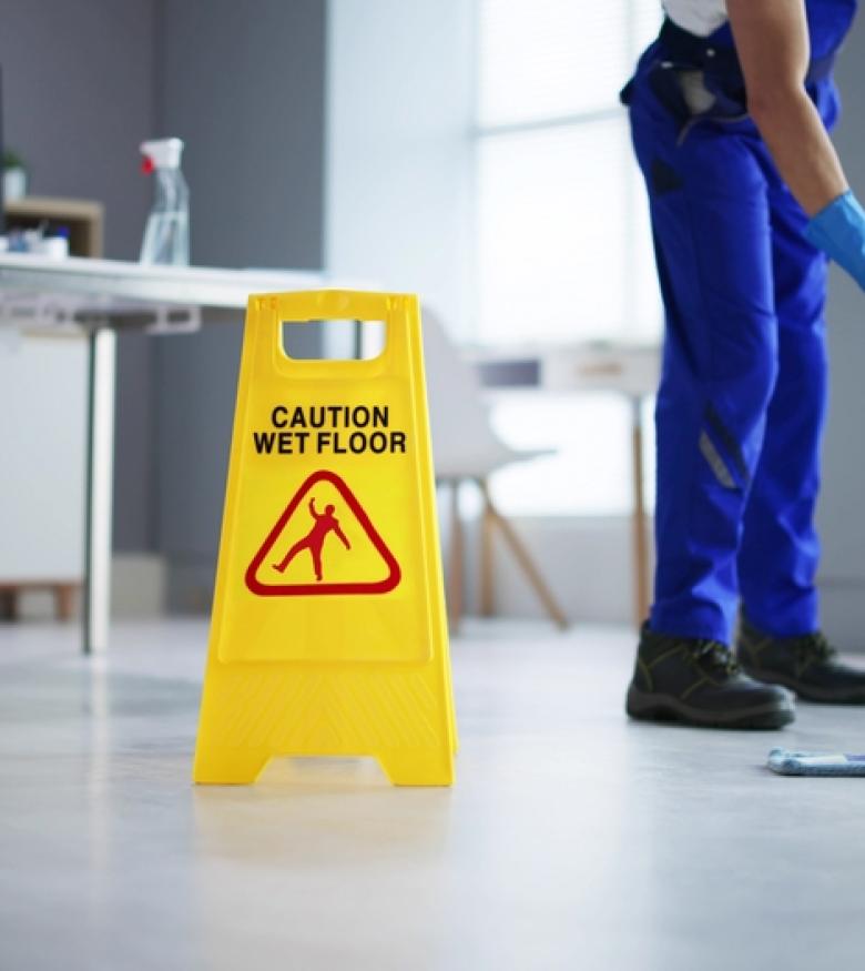 Janitor mopping floor next to yellow caution wet floor sign in office setting