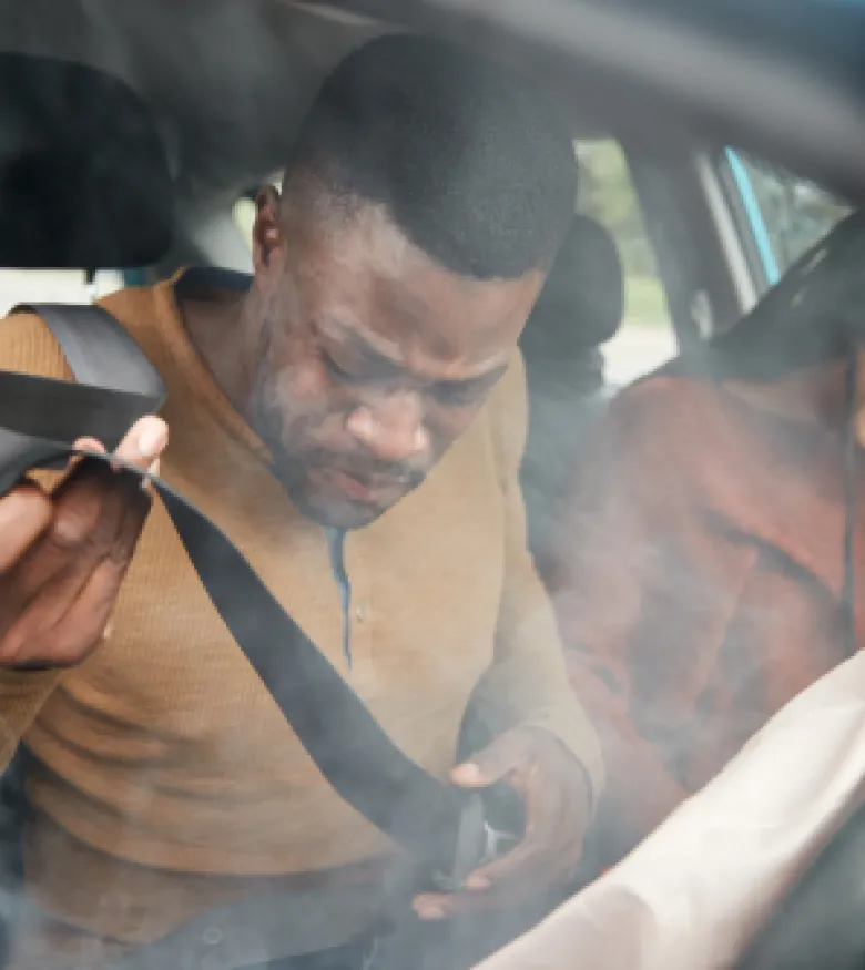 Man and woman experiencing airbag injuries in Indianapolis after a car accident, with airbags deployed and visible smoke inside the vehicle.