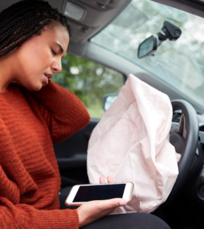 A woman holding her neck in pain while looking at a deployed airbag inside a car after an accident, representing airbag injuries in Orange Park.