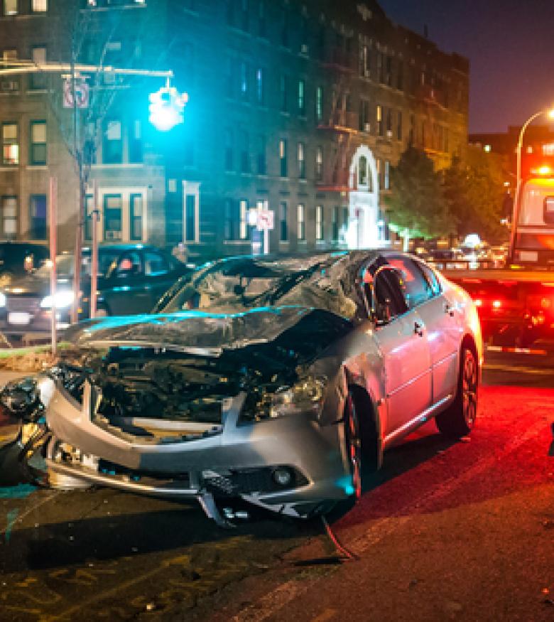 A damaged car on the street with a tow truck in the background, illustrating the need for a Car Wreck Lawyer in Augusta.