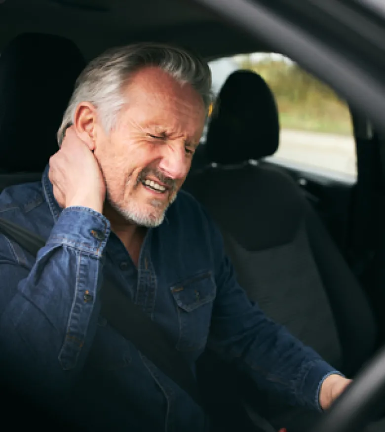 Man sitting in a car holding his neck in pain after an accident, highlighting airbag injuries in Hilton Head Island.