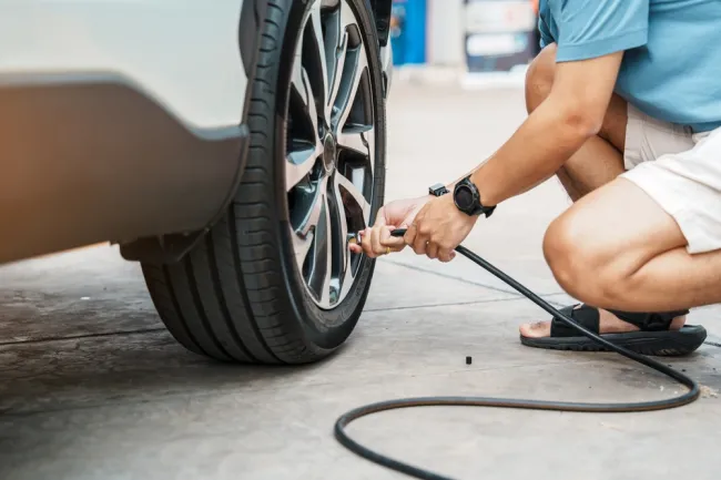Person inflating a car tire with an air pump, ensuring proper tire maintenance and safety