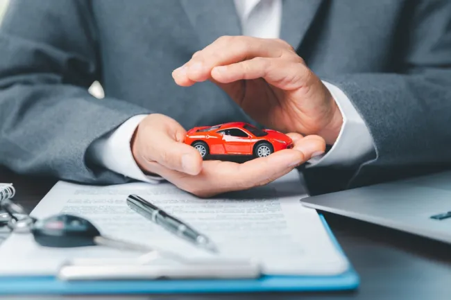 Insurance agent protecting a red toy car with hands, symbolizing car insurance and coverage consultation