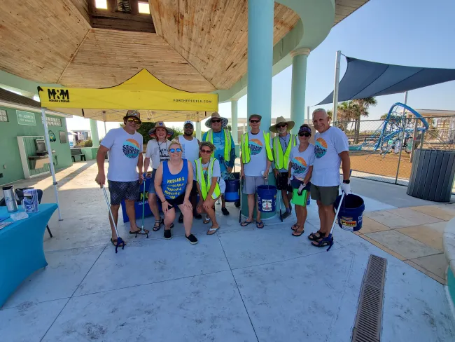 Group of volunteers from Morgan & Morgan participating in a beach and park cleanup event for World Oceans Day under a yellow M&M tent.