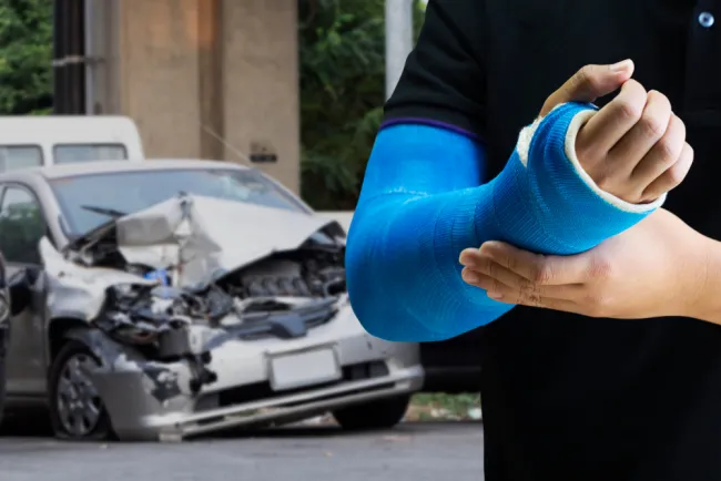 Man with an arm cast standing in front of a damaged car