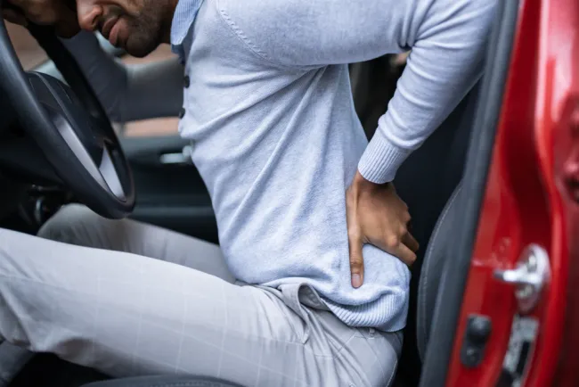 Man holding back in pain sitting in a car