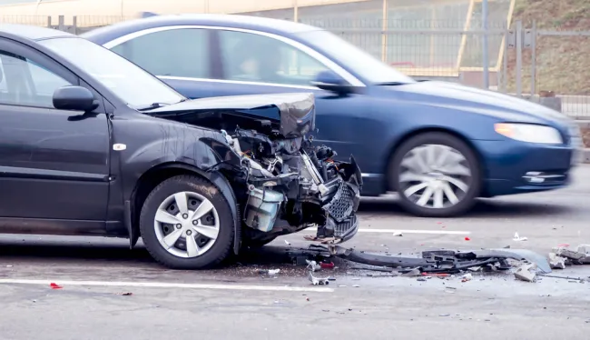 Car with lots of damage to its front end and another car driving by