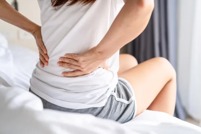 Women sitting on edge of bed holding back in pain 