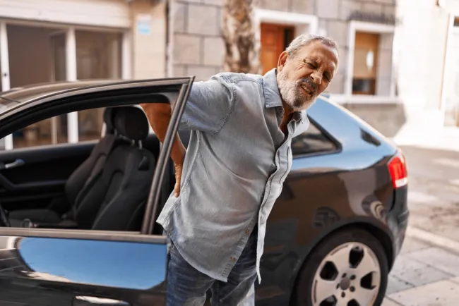 Elderly man getting out of a car holding his back in pain 