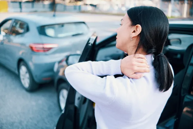 Woman holding her neck in pain standing outside of a car