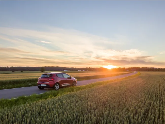 Car driving down a road with a sunset in the background