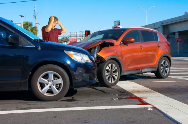 Orange and blue car crashed into each other with a man standing nearby in shock